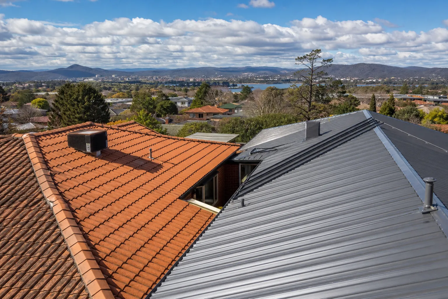 A Canberra street with a concrete-tile roof beside a modern Colorbond steel roof under a frosty winter sky